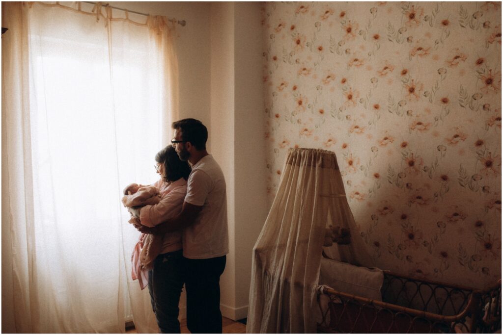 Parents tenant leur bébé devant la fenêtre lors d'une séance photo naissance à toulouse.