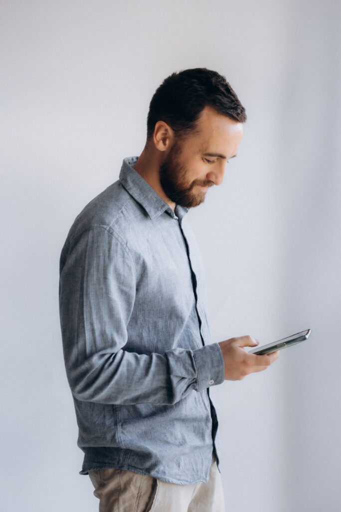 Un homme debout en chemise bleue qui regarde son smartphone.