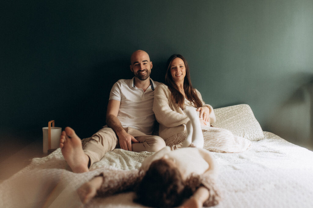 Un homme et une femme assis sur un lit en train de regarder leur enfant.