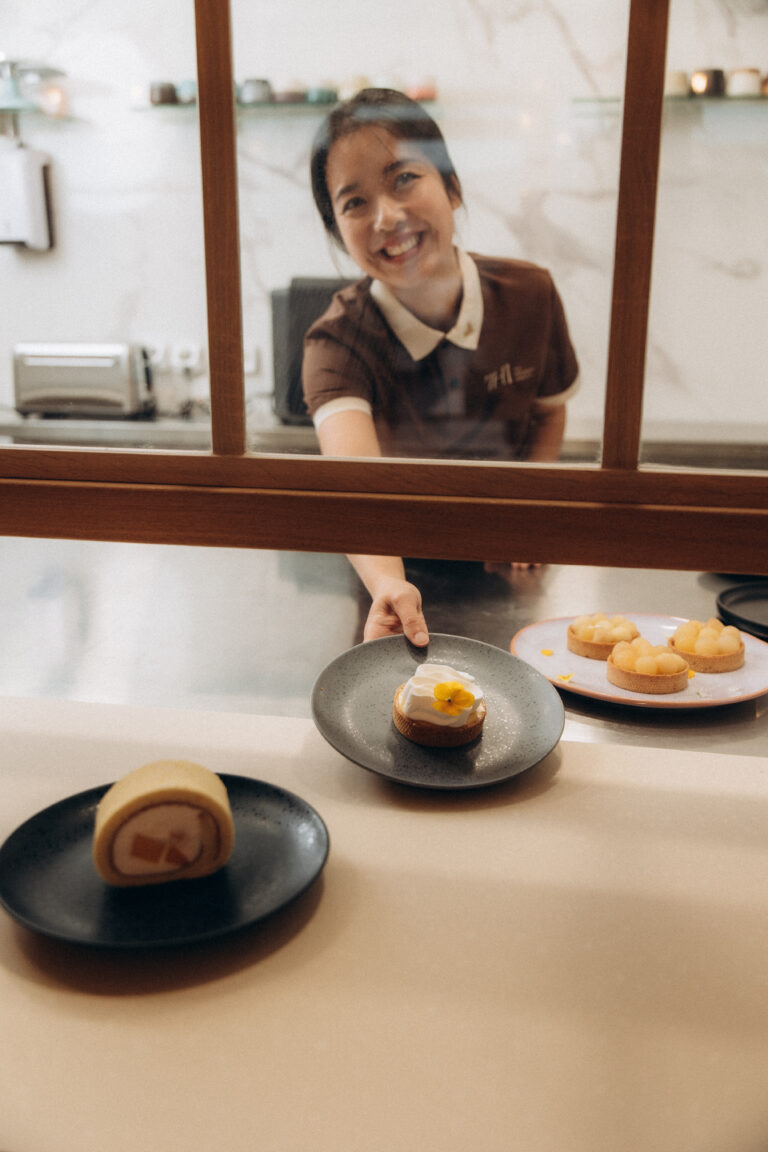Une femme derrière une verrière tend une assiette avec une pâtisserie dedans.