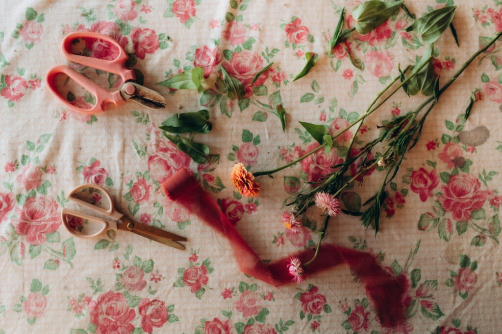 Des outils de fleuriste disposés sur une nappe fleuris, à plat.