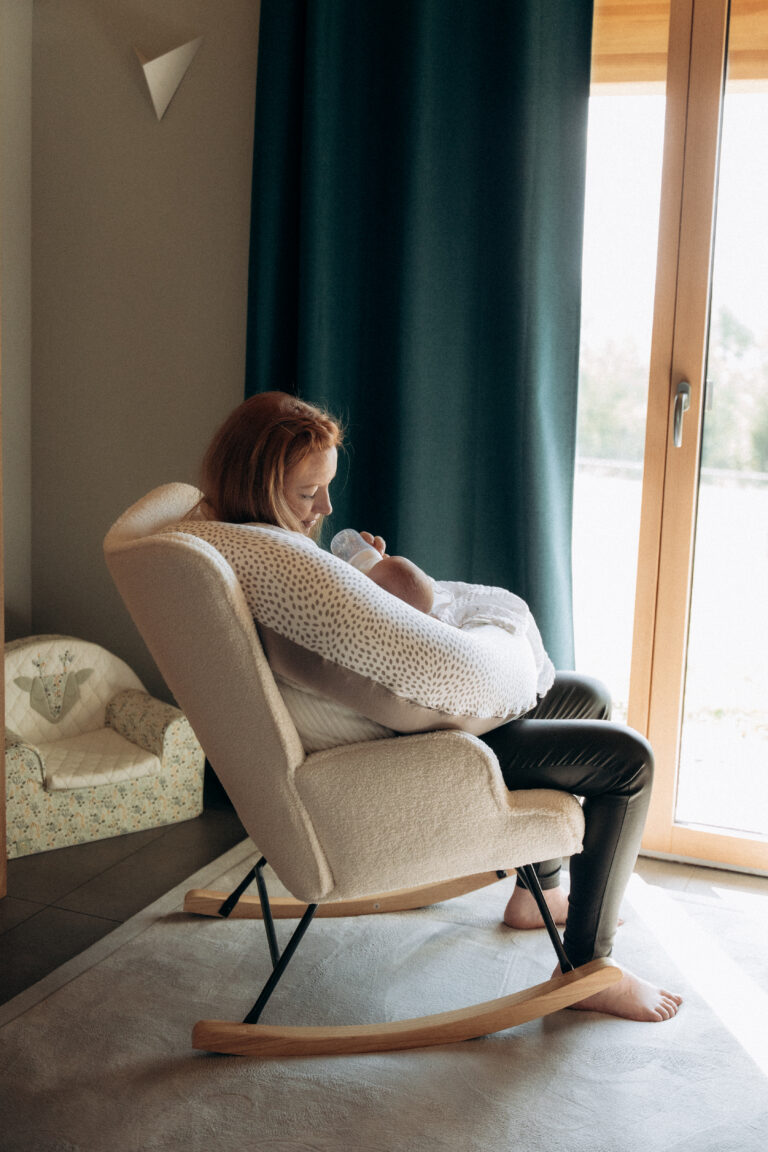 Une maman assise dans un fauteuil. Elle donne le biberon à son bébé.