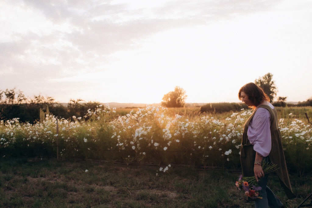 Une femme marche au milieu d'un champ de fleurs au coucher du soleil.