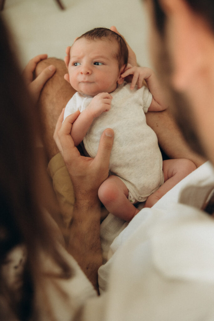 Un bébé tenu sur les genoux de son papa. Ses yeux sont ouverts.
