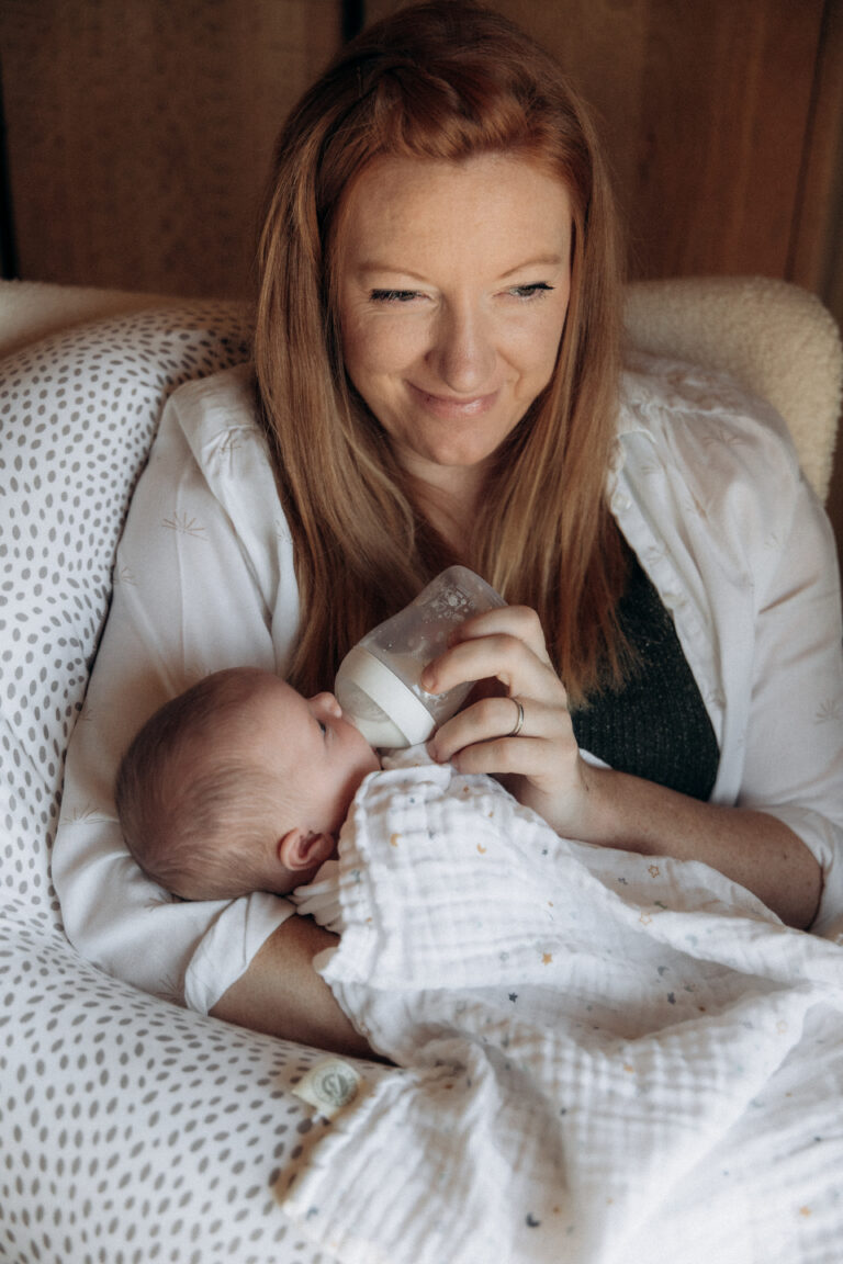 Une maman qui sourit. Elle tient dans ses bras un bébé et lui donne le biberon.