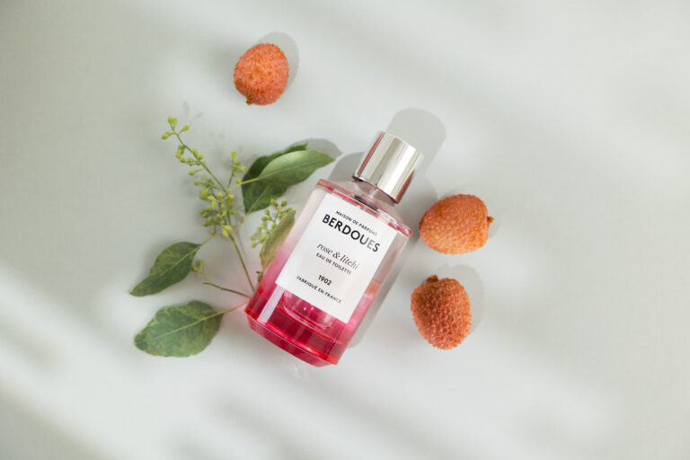 Un parfum rose posé sur le sol entouré de litchi et de petites feuilles vertes.