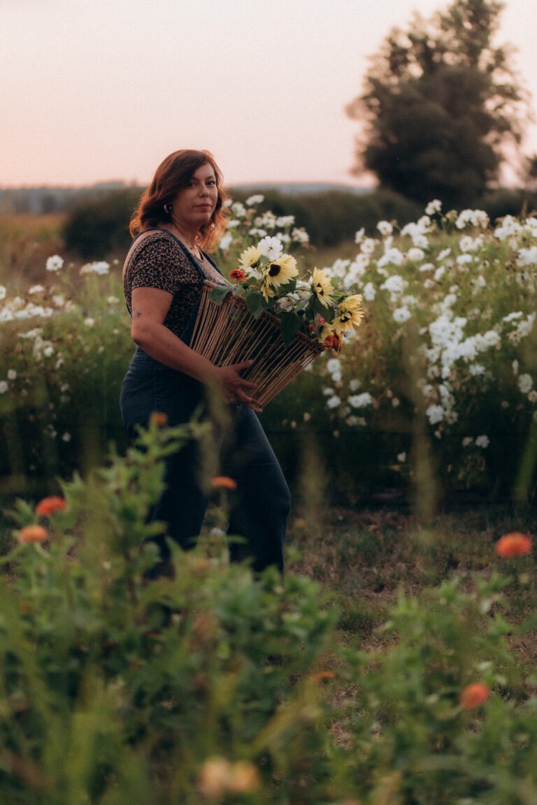 Une femme tenant un seau remplit de fleurs et se tenant au milieu d'un champ de fleurs.