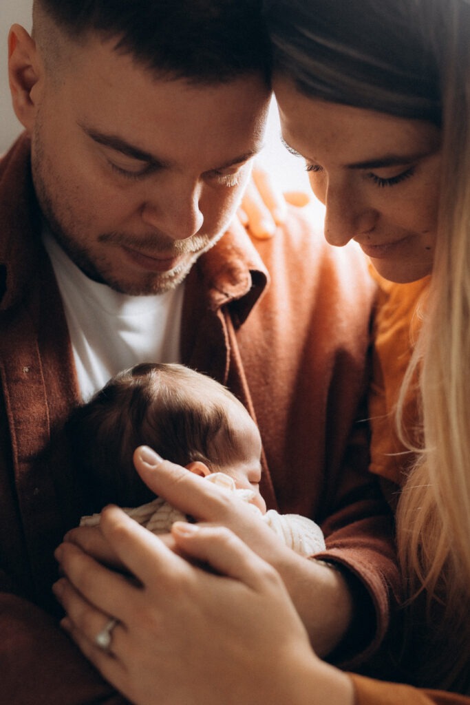 Un papa et une maman accolé et tenant leur nourrisson dans les bras.