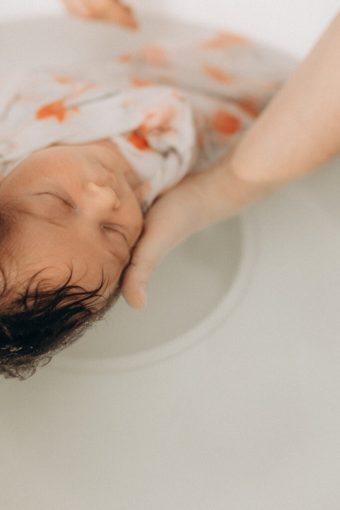 Un bébé dans le bain soutenu par une main.