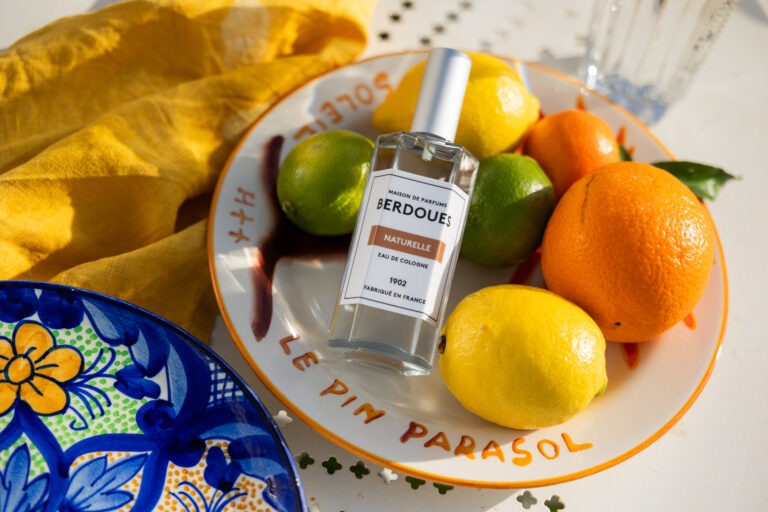 Un parfum posé sur des agrumes et dans une assiettes colorés.