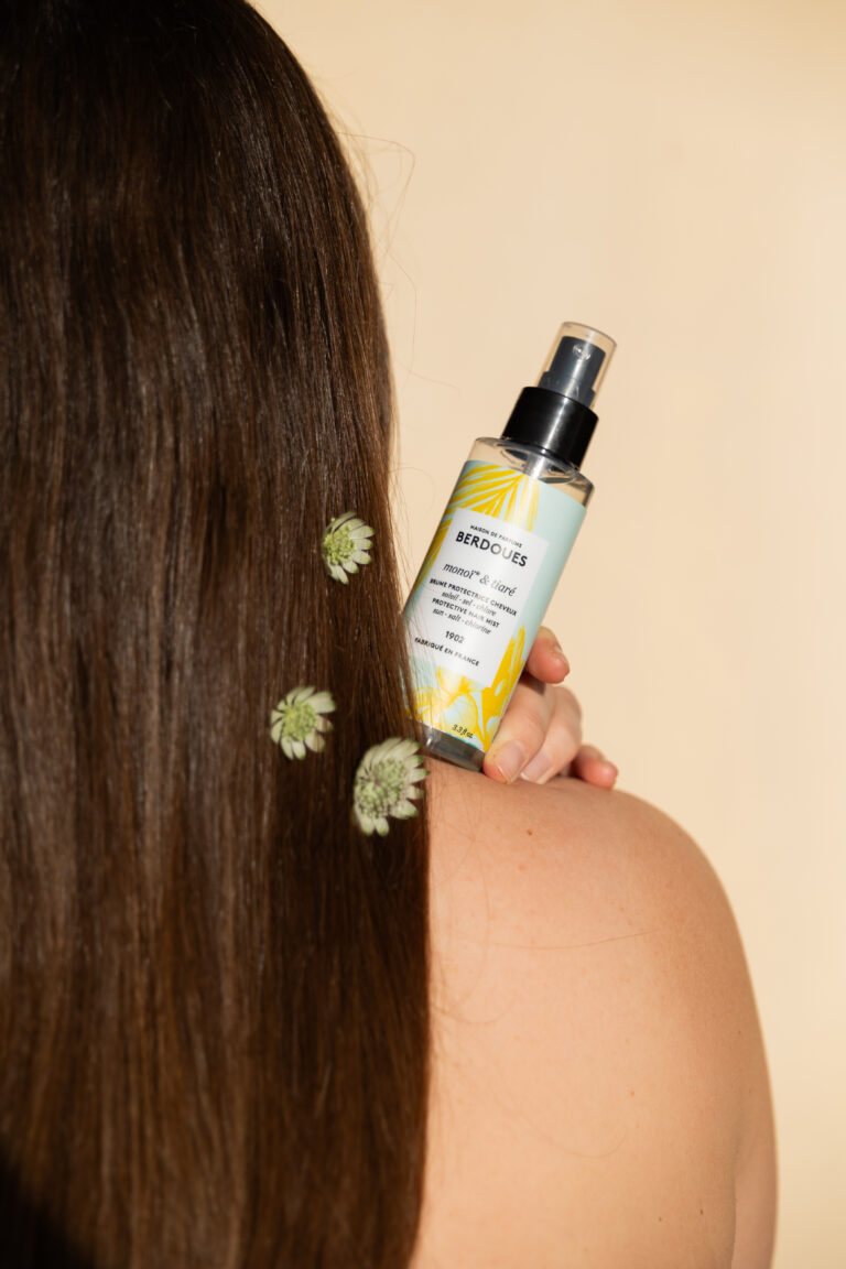 Un produit de beauté posé sur une épaule dénudée de femme et entouré de cheveux.