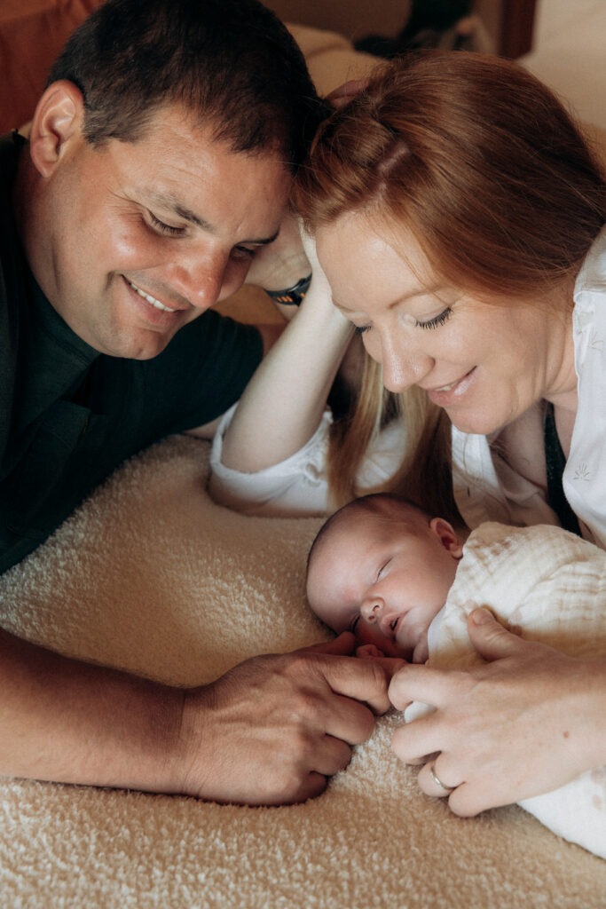 Un papa et une maman qui entourent leur bébé endormi.