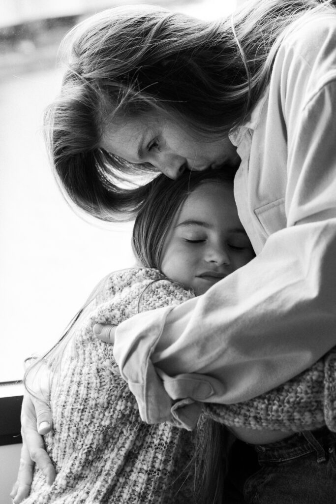 Une maman embrasse sa fille sur le front et lui fait un câlin.