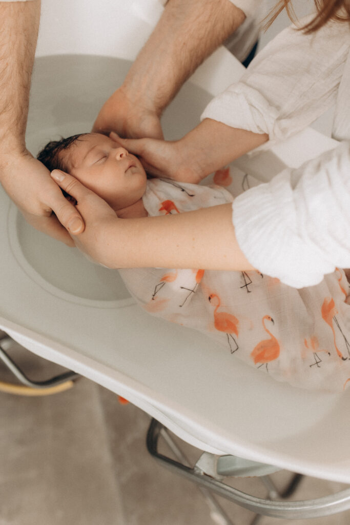 Un bébé dans le bain et tenu par les bras de ses parents.