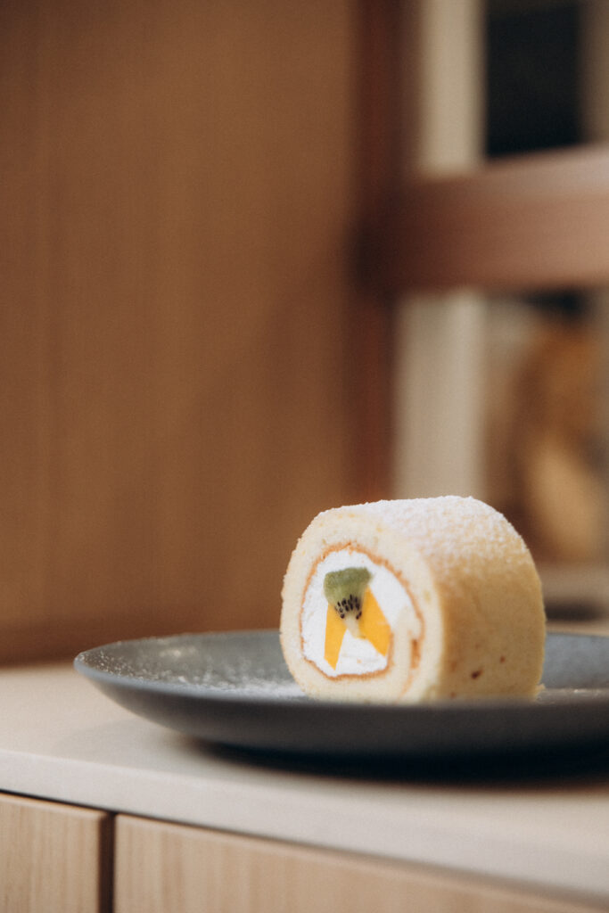 Une pâtisserie ronde et blanche avec des morceaux de mangues disposée sur une assiette grise.