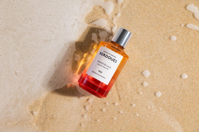 Un parfum orange posé sur le sable avec une vague.