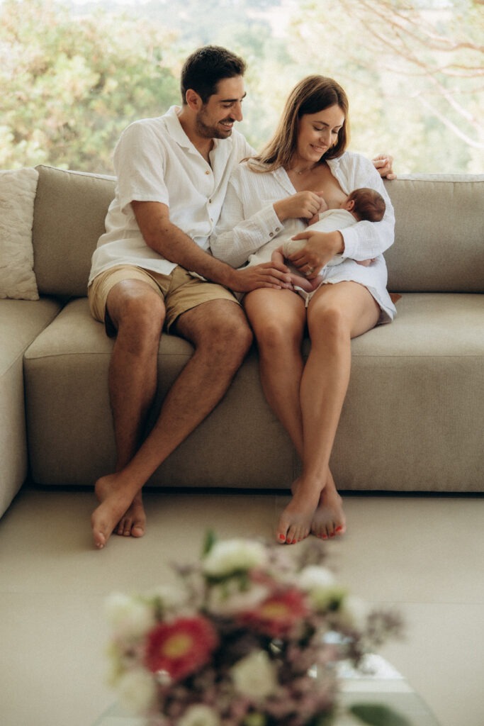 Un papa et une maman assis sur un canapé beige, tenant dans leurs bras leur bébé.