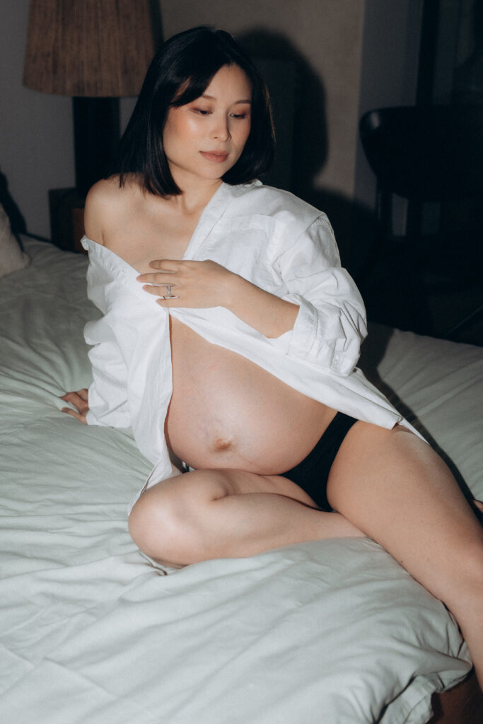 Une femme aux traits asiatiques et enceinte est assise sur un lit.